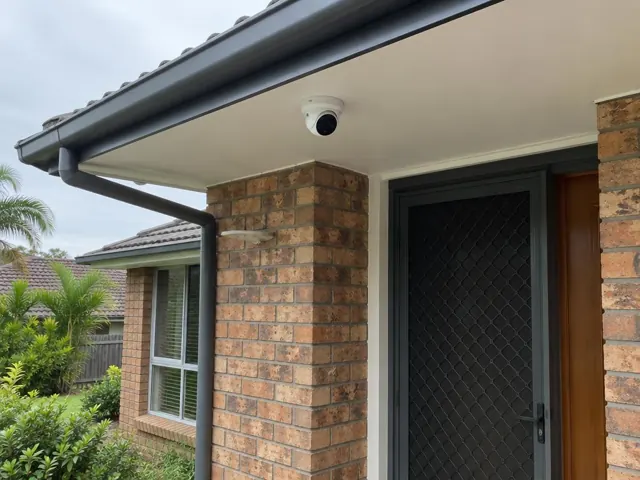 White dome CCTV camera mounted under an exterior eave above a brick entry in Helensvale