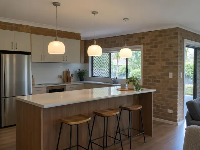 Three pendant lights over a kitchen island in a brick-walled home interior in Maudsland